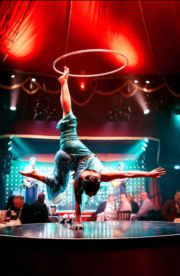 Female performer balancing on her hand while spinning hula hoop on foot during hula hoop dance performance | Altus Entertainment